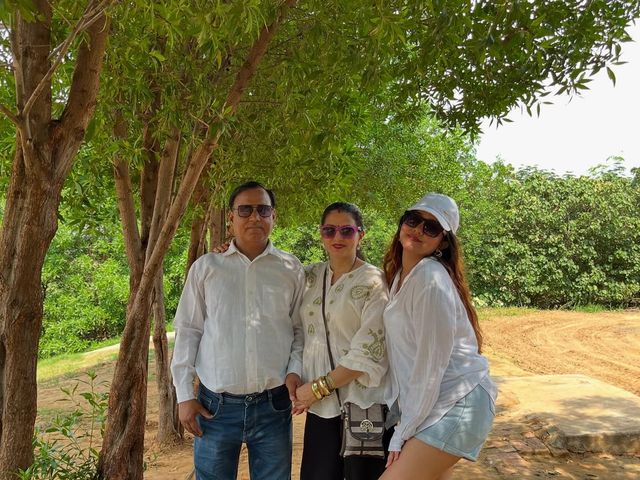 A family in white posing under a shady tree during a day outing at Rangmanch Farms, an outdoor venue in Gurugram near Delhi