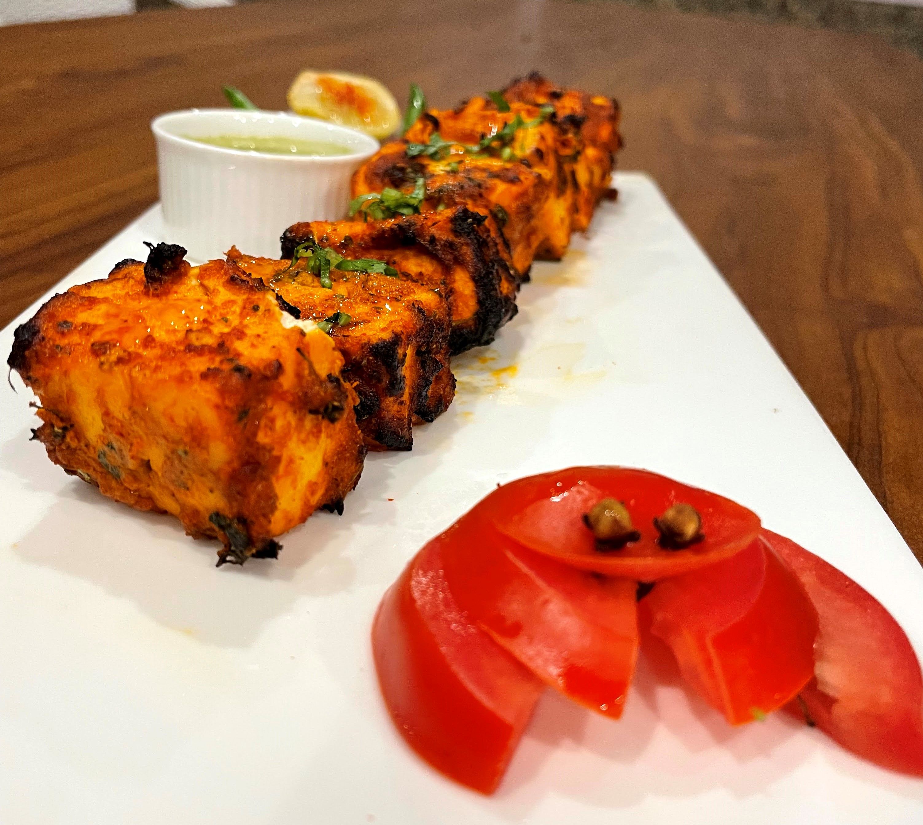 Grilled paneer tikka starters served with green chutney, lemon and sliced tomato on a white platter from the starters counter at Rangmanch Farms, Gurugram