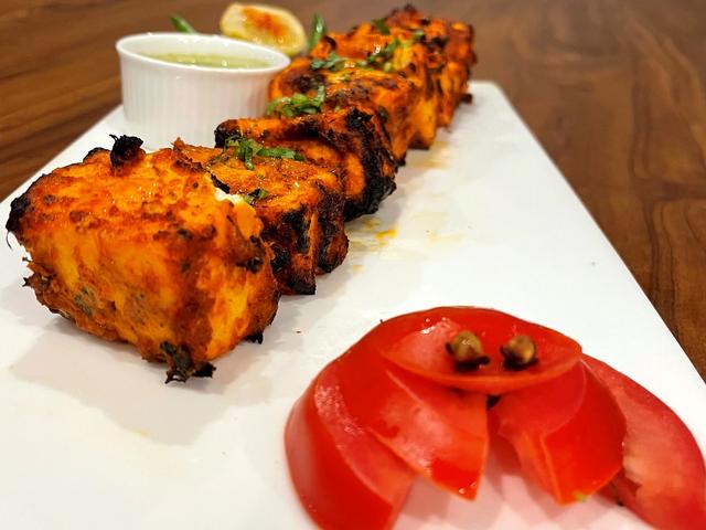 Grilled paneer tikka starters served with green chutney, lemon and sliced tomato on a white platter from the starters counter at Rangmanch Farms, Gurugram
