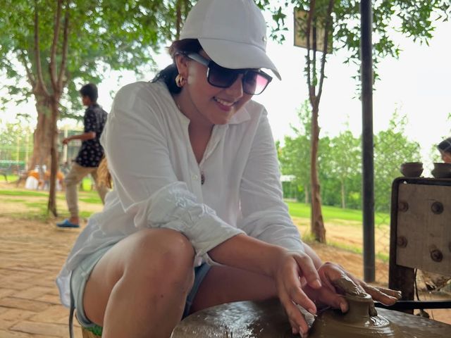 A smiling guest in a cap and sunglasses shaping wet clay at a pottery wheel during an outdoor activity at Rangmanch Farms, Gurugram near Delhi
