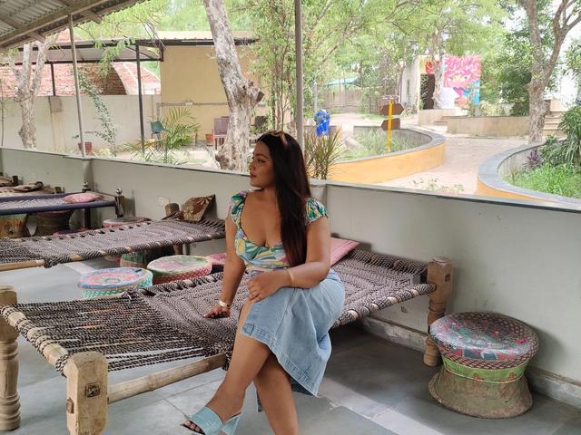 Woman seated on a traditional woven charpai in a shaded rustic seating area overlooking the greenery at Rangmanch Farms, an outdoor day outing venue in Gurugram near Delhi