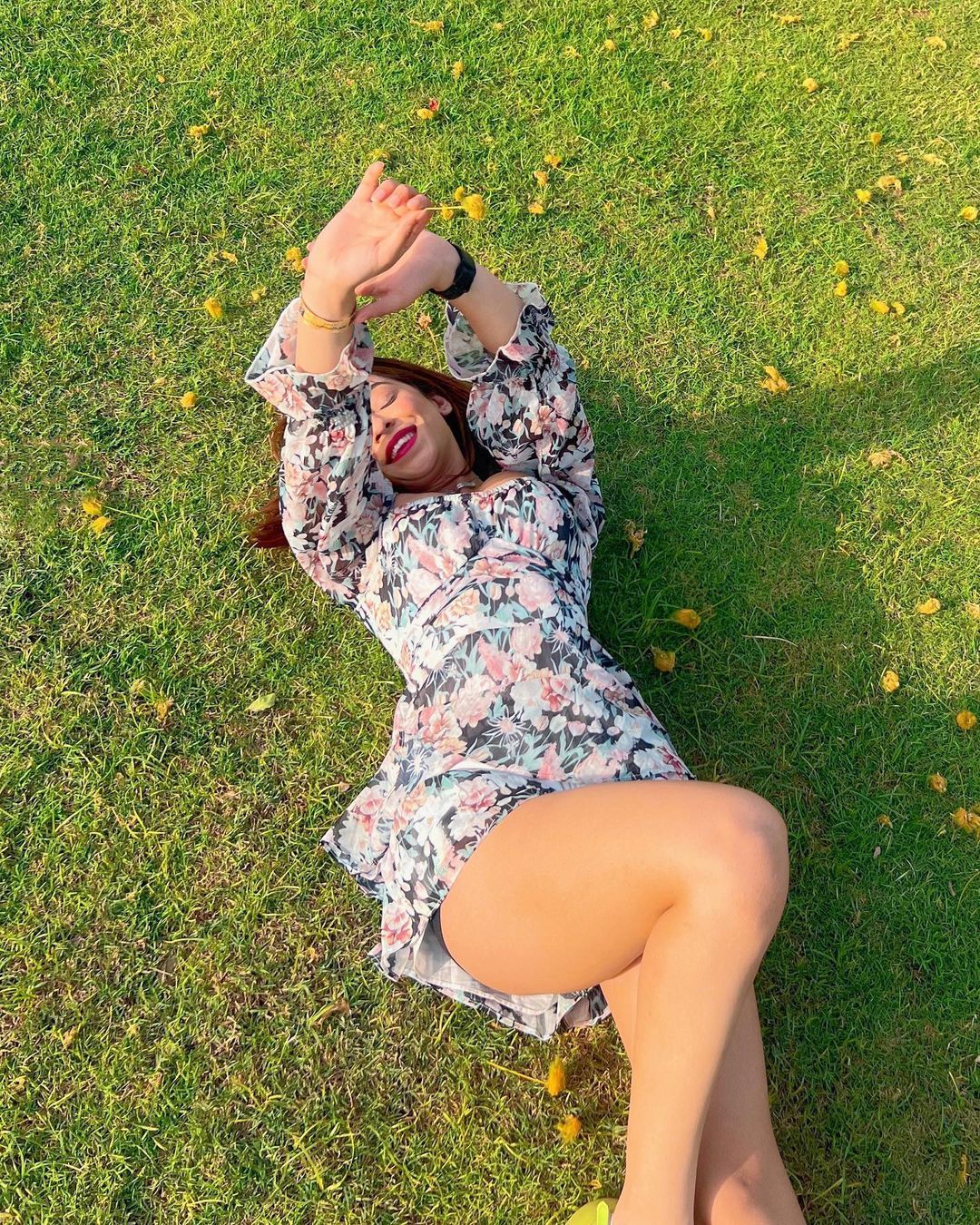 Woman in a floral dress lying on the grass lawn scattered with fallen flowers during a day outing at Rangmanch Farms, an outdoor venue in Gurugram near Delhi