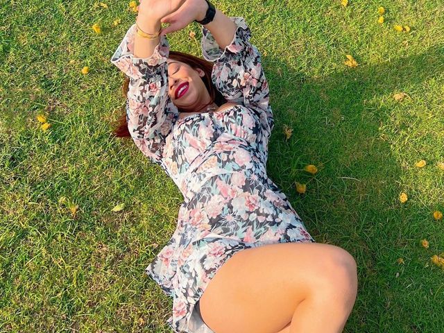 Woman in a floral dress lying on the grass lawn scattered with fallen flowers during a day outing at Rangmanch Farms, an outdoor venue in Gurugram near Delhi