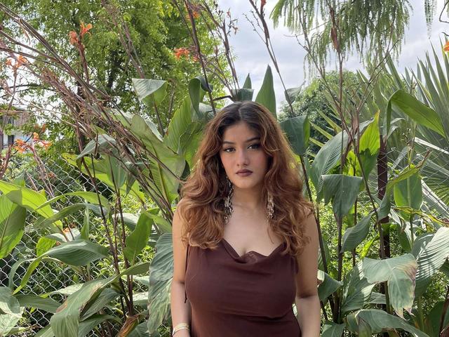 Woman in a brown dress posing beside flowering plants and tall foliage in the garden at Rangmanch Farms, an outdoor event venue in Gurugram near Delhi