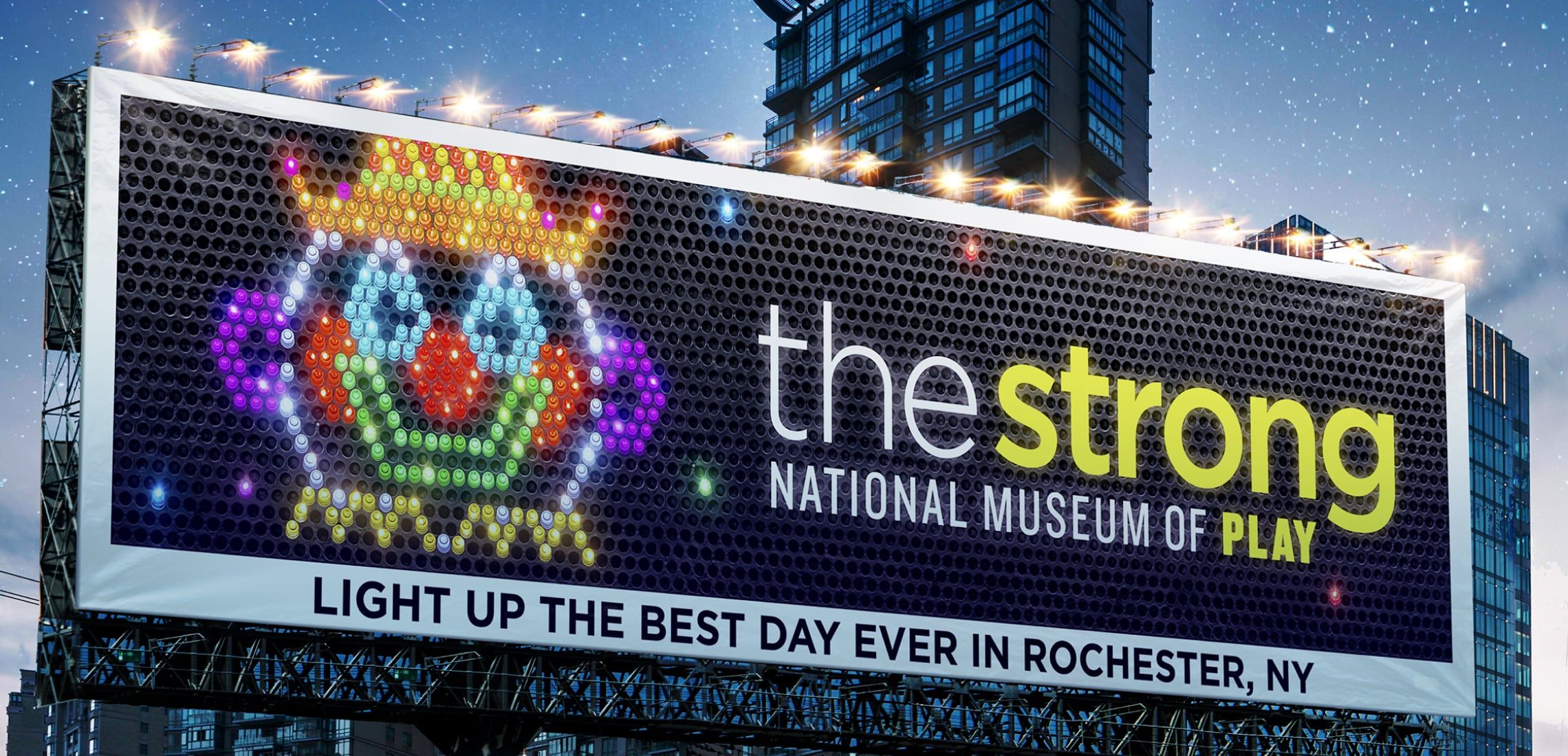 Photograph of a Strong National Museum of Play billboard that looks like a clown's face made on a Lite Brite. It says, "Light up the best day ever in Rochester, NY."