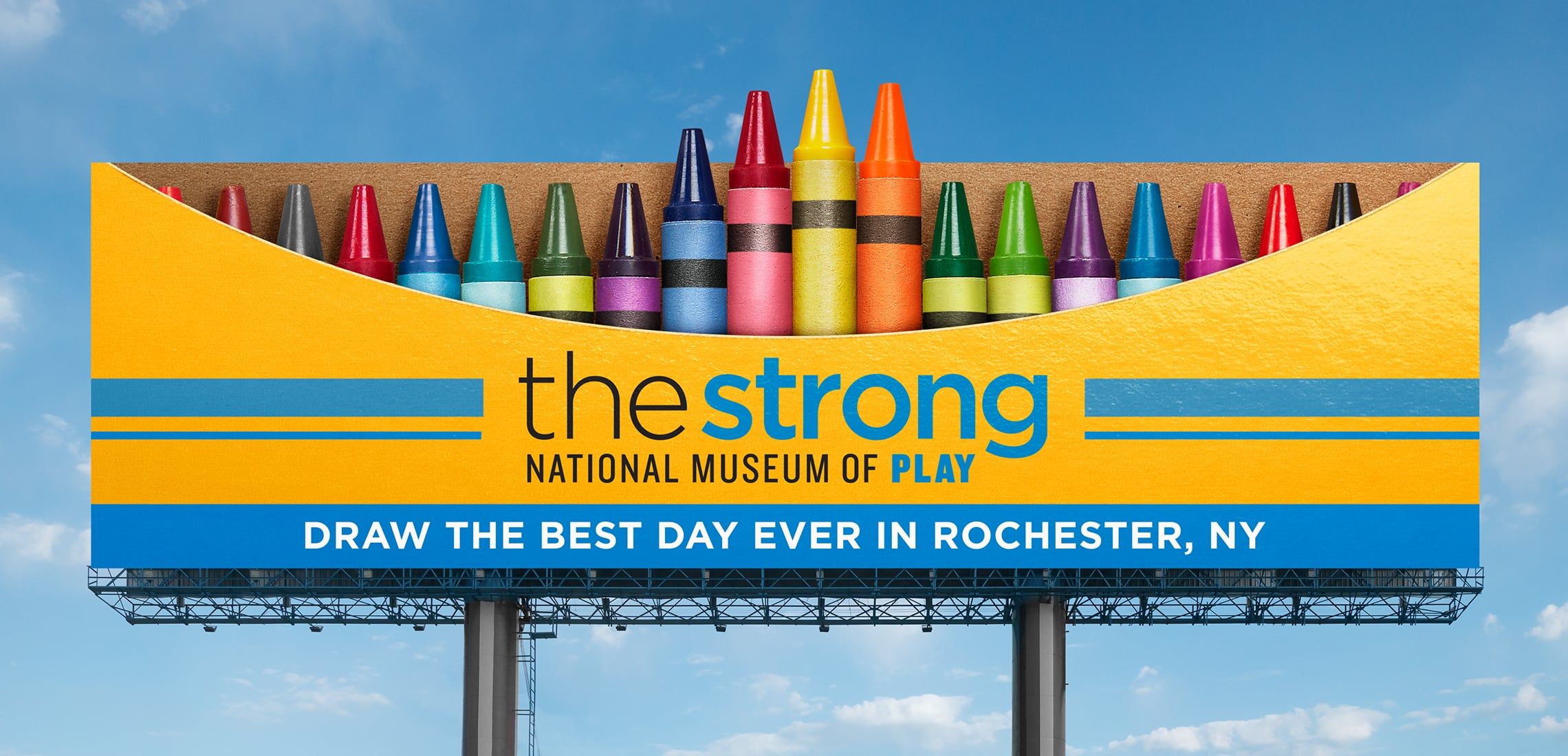 Photograph of a Strong National Museum of Play billboard that looks like an open box of crayons. It says, "Draw the best day ever in Rochester, NY."