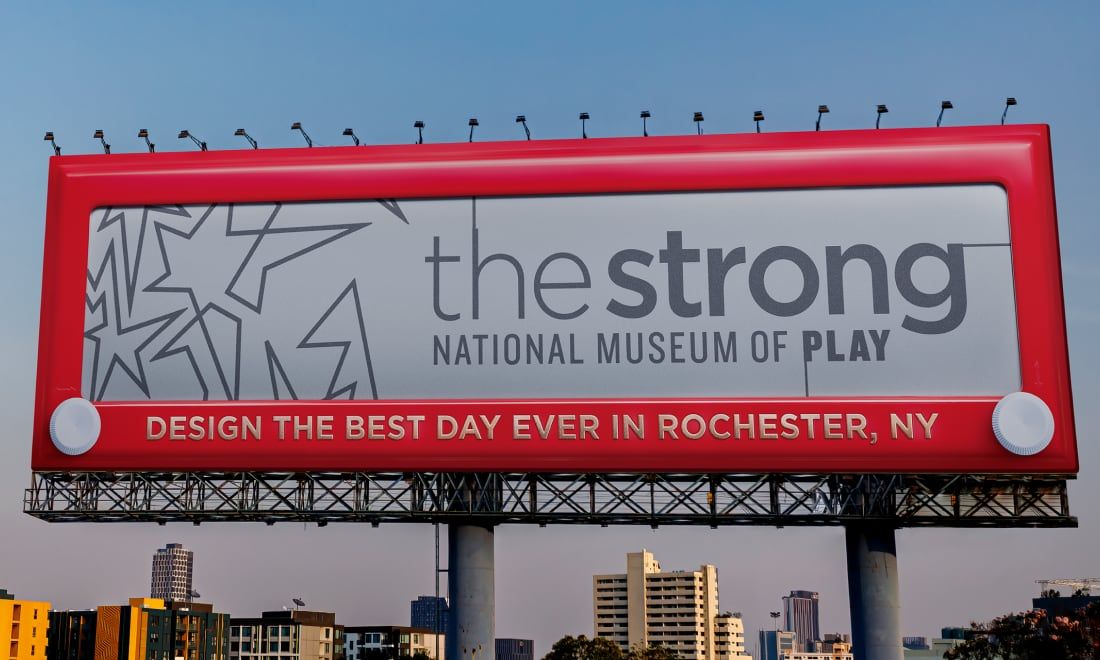 Photograph of a Strong National Museum of Play billboard that looks like an Etch-a-Sketch. It says, "Design the best day ever in Rochester, NY."