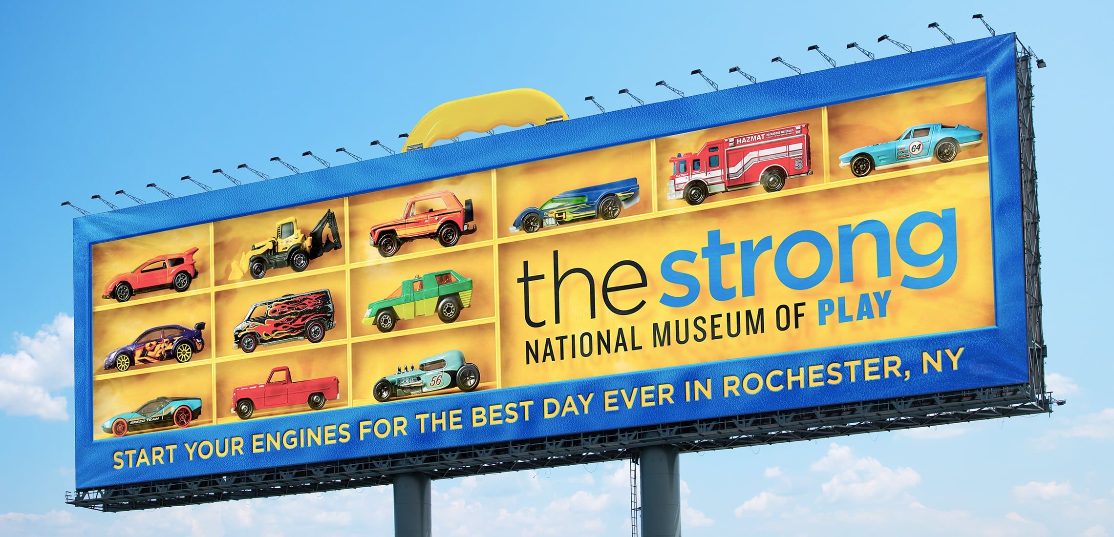 Photograph of a Strong National Museum of Play billboard that looks like an box to store Hot Wheels toy cars. It says, "Start your engines for the best day ever in Rochester, NY."