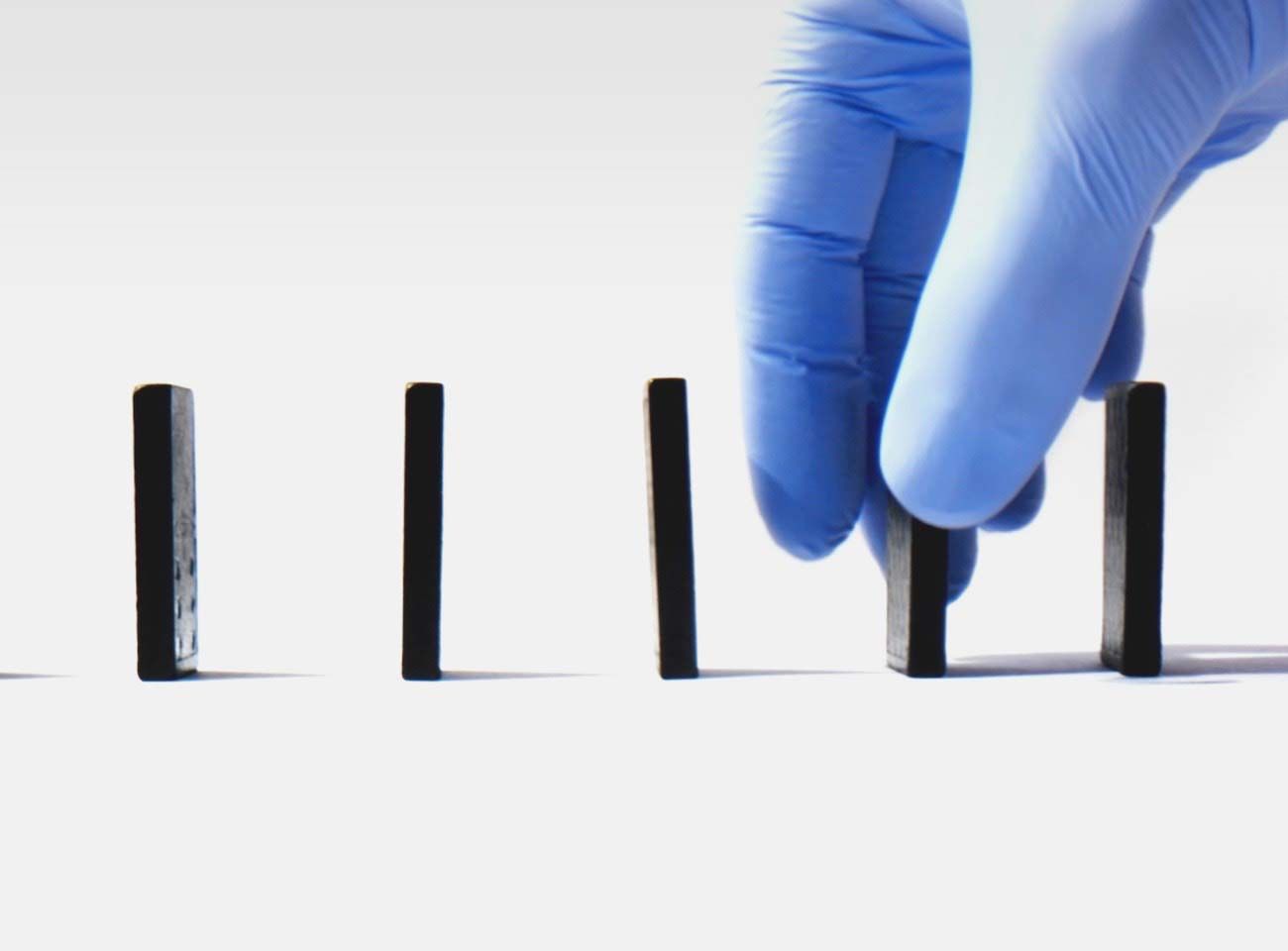 A hand in medical gloves grabbing a domino from a line. Click to view the video.