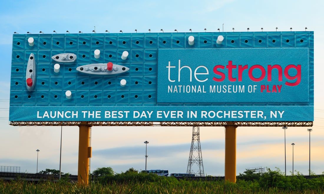 Photograph of a Strong National Museum of Play billboard that looks like the board game Battleship. It says, "Launch the best day ever in Rochester, NY."