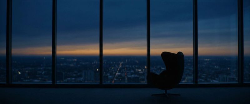 An armchair silhouetted against a window over a city at dusk