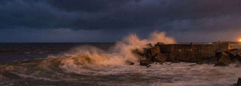 A concrete breakwater absorbing a heavy wave at dusk