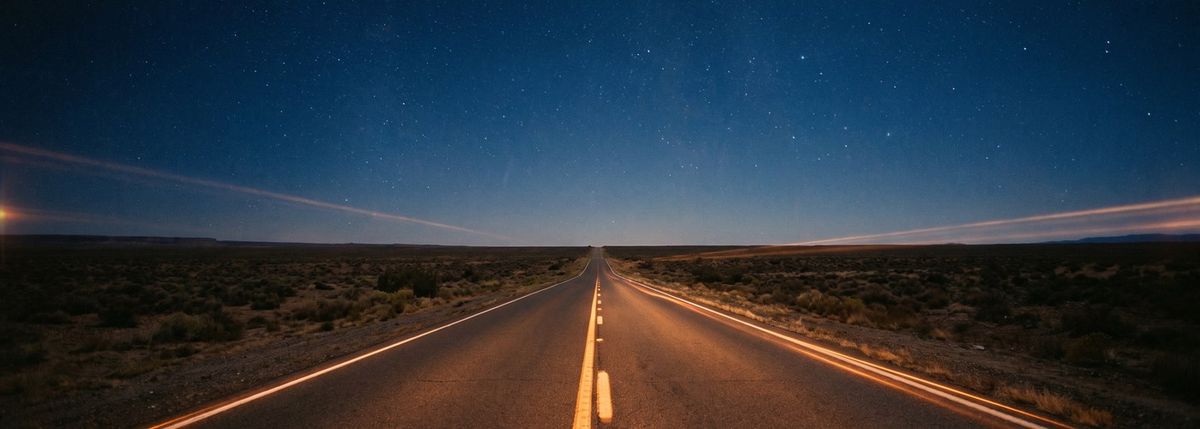 An empty desert highway at night receding under a starlit sky