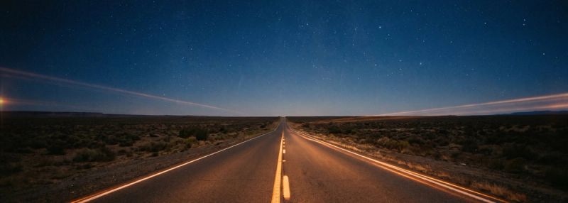 An empty desert highway at night receding under a starlit sky
