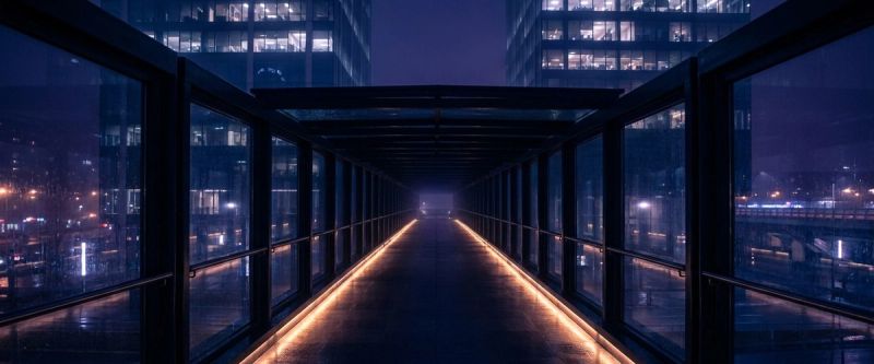 A glass corridor bridge between two office towers at night