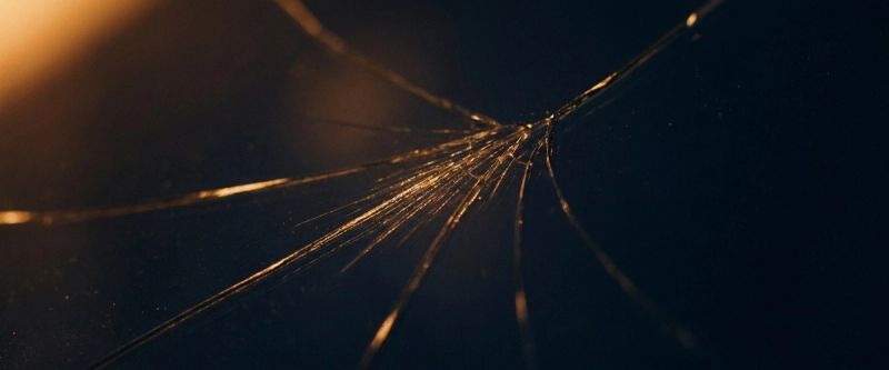 A fine crack radiating across dark glass in raking light