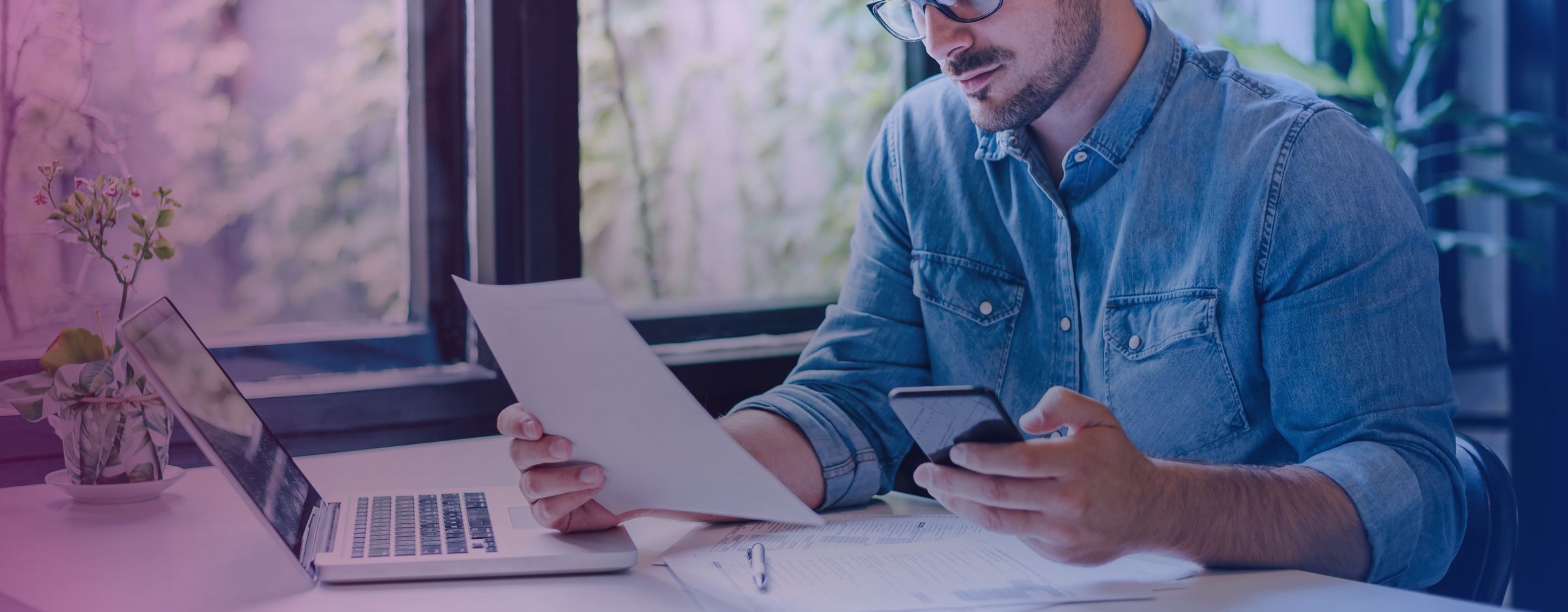 A person working out their accounts using their laptop, phone and paper