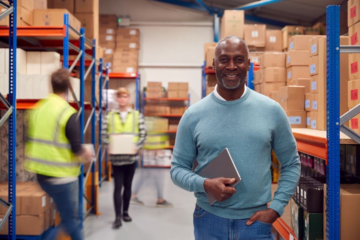 Man with notebook standing in a busy warehouse
