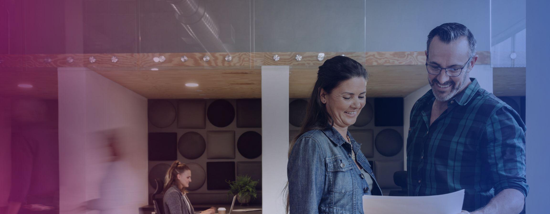 Man and woman talking at a desk in a busy office