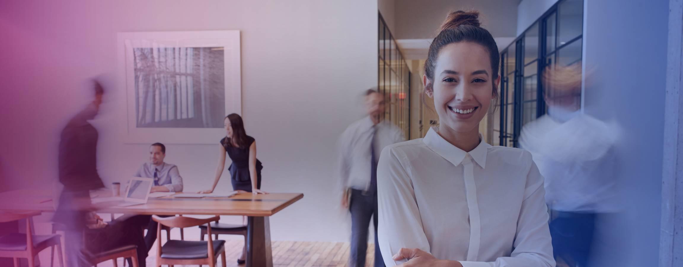 Kvinde, der smiler til kameraet på et travlt kontor