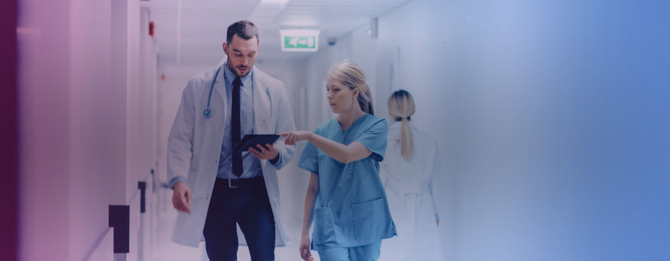 NHS workers walking down a corridor in conversation pointing at an electronic tablet
