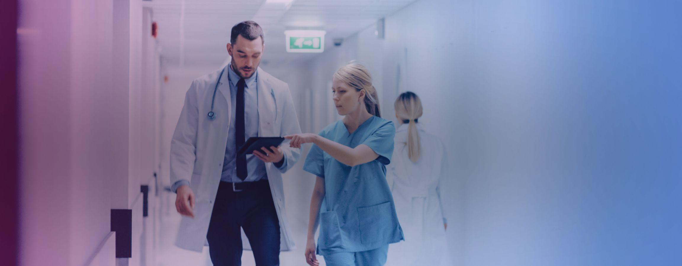 NHS workers walking down a corridor in conversation pointing at an electronic tablet