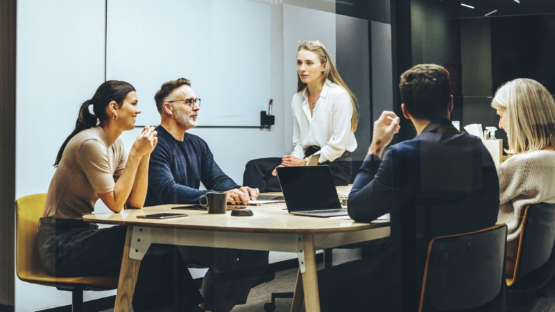 A stock image of an office with employees having a discussion at a table