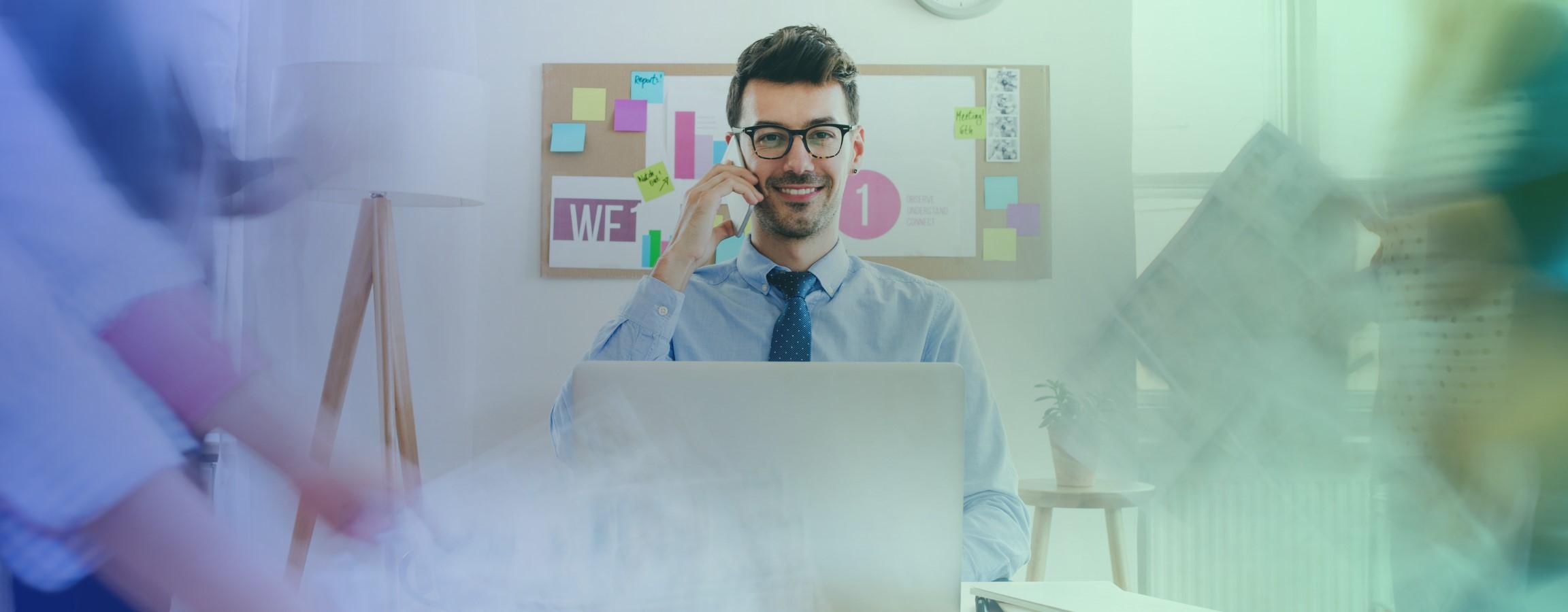 An office stock image with an employee on his laptop and smiling at the camera