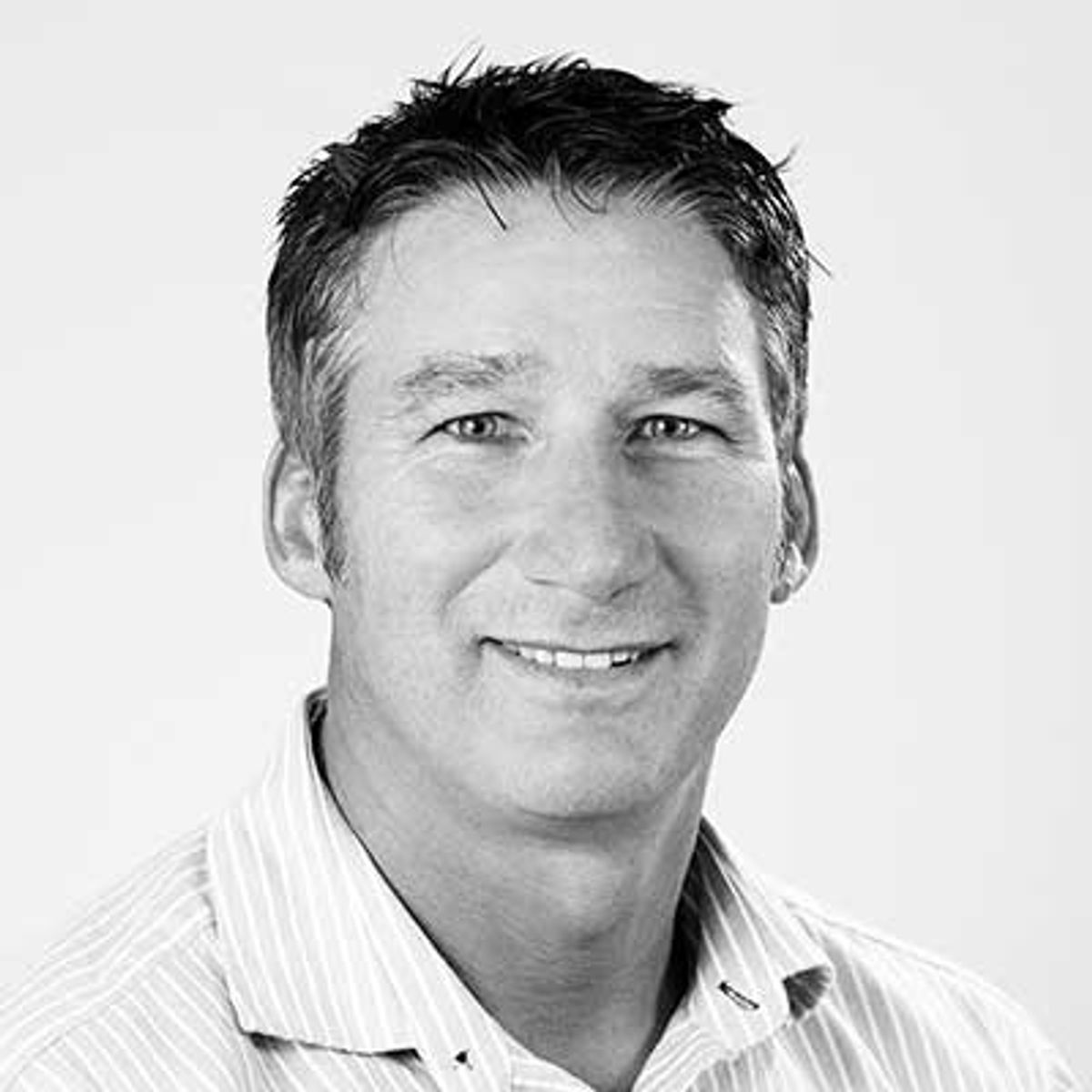 Black and white headshot of a smiling middle-aged man wearing a striped shirt.
