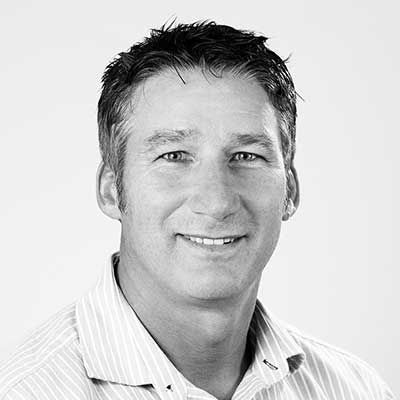 Black and white headshot of a smiling middle-aged man wearing a striped shirt.