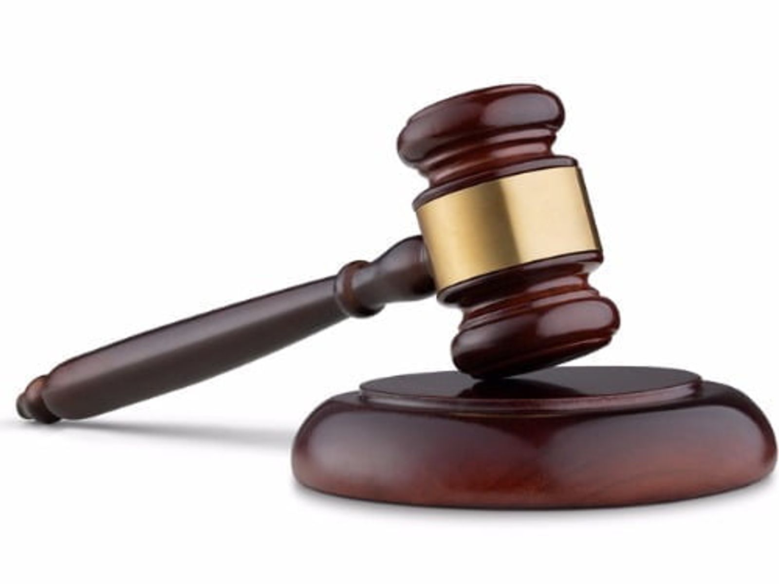 Wooden judge's gavel with brass band resting on round sound block.