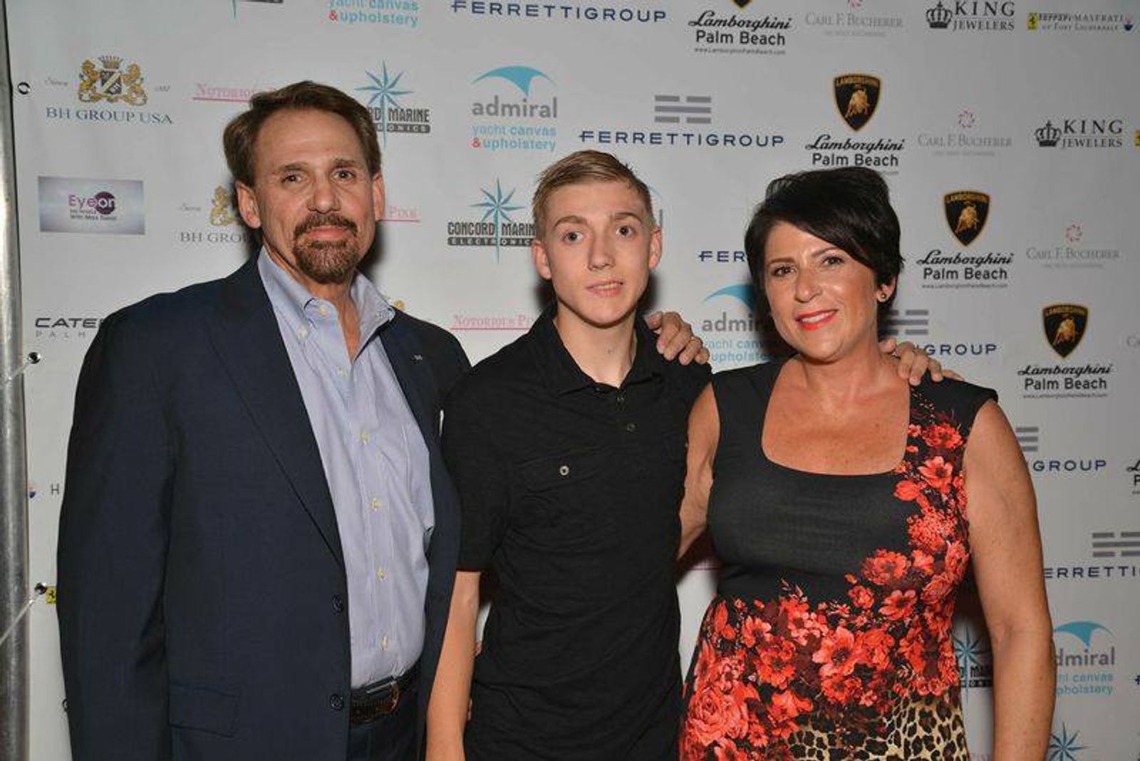 Three people posing at event with branded backdrop featuring Lamborghini and Admiral logos.
