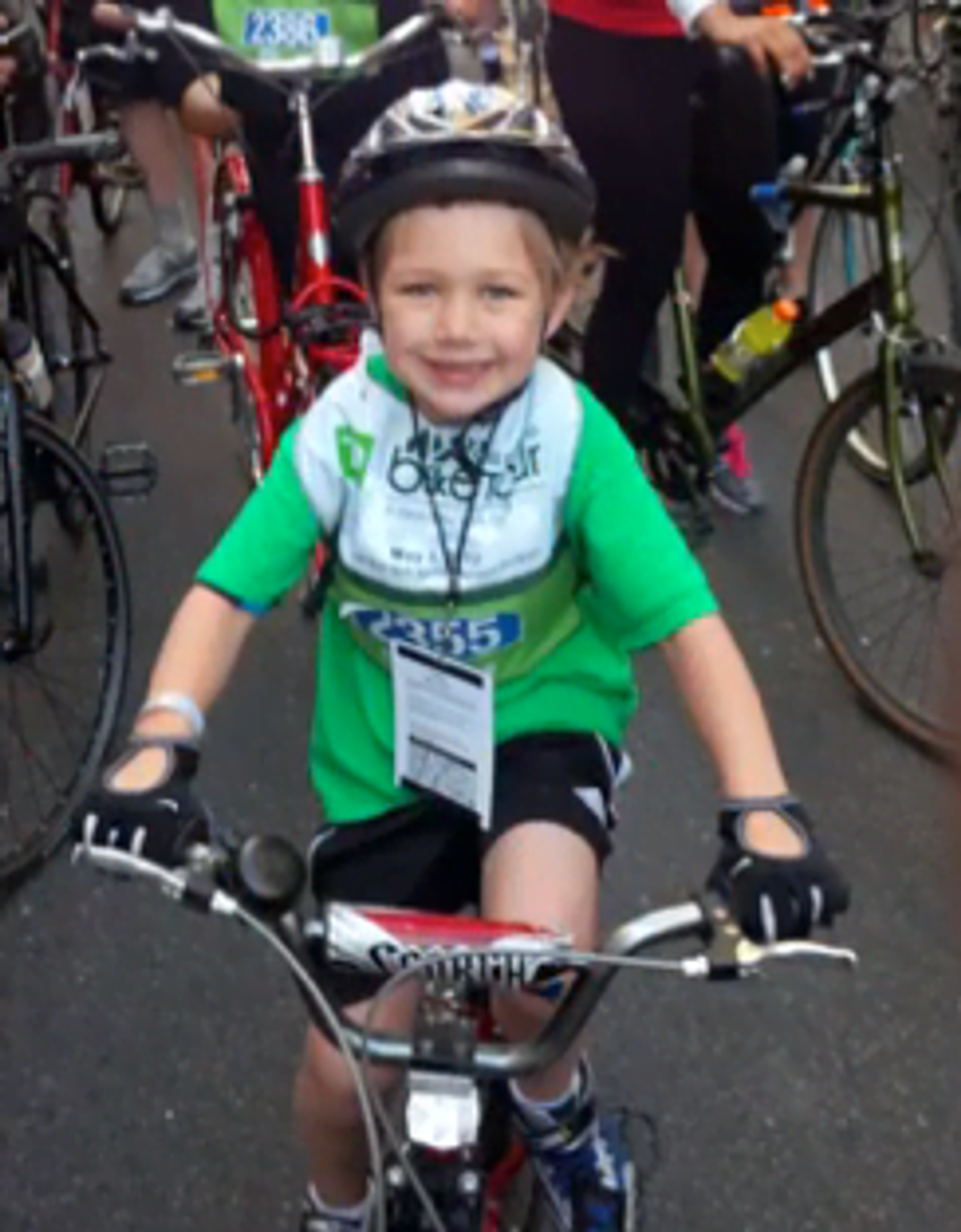 Young child on red bicycle wearing green jersey and helmet at cycling event