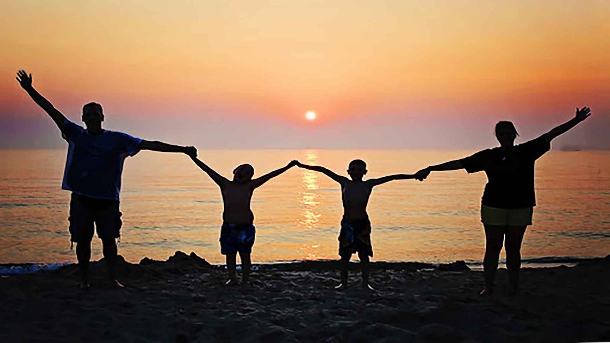 Silhouettes of five people holding hands on beach at sunset.