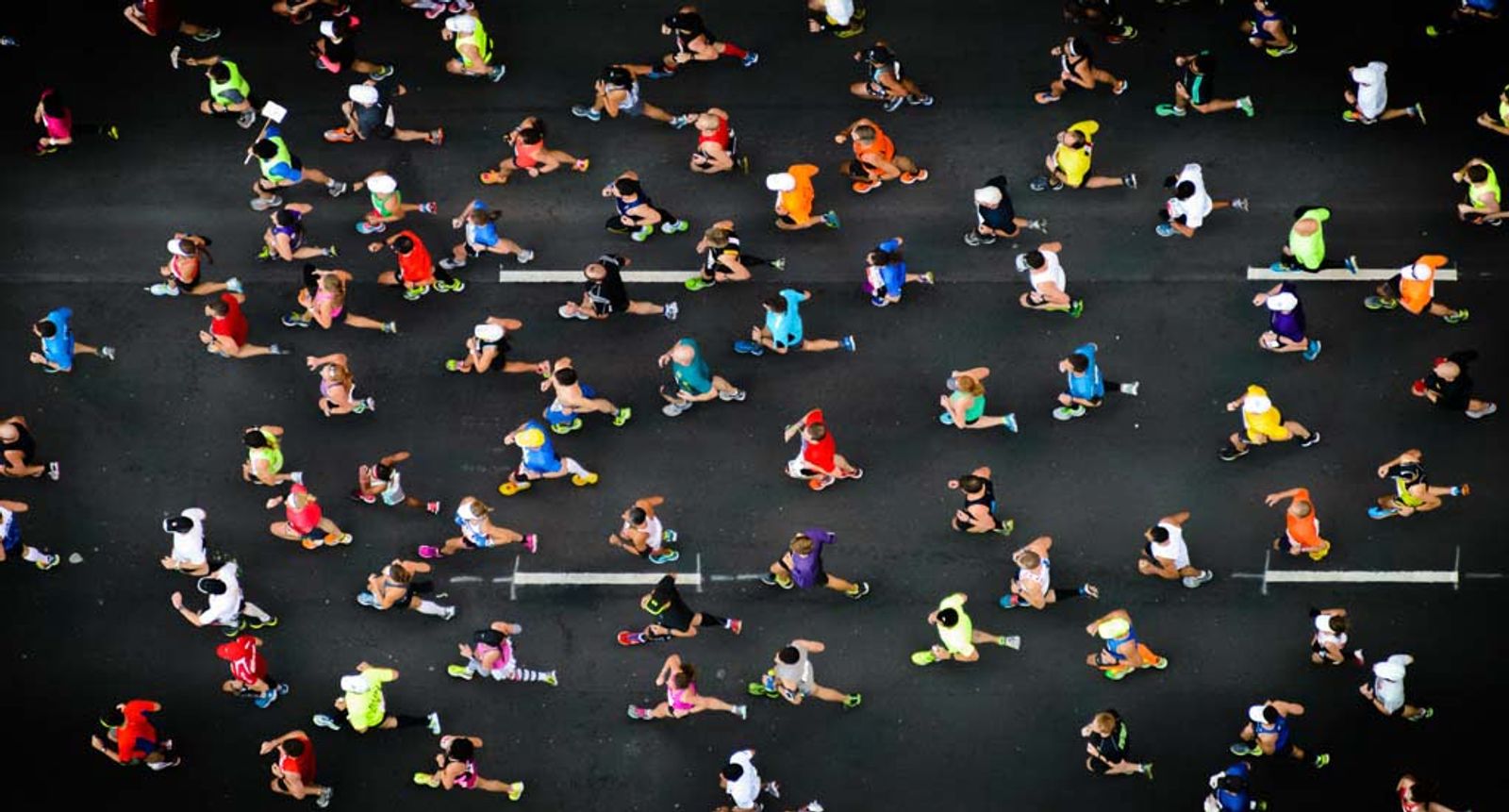 Aerial view of numerous people exercising on dark pavement with white line markings.