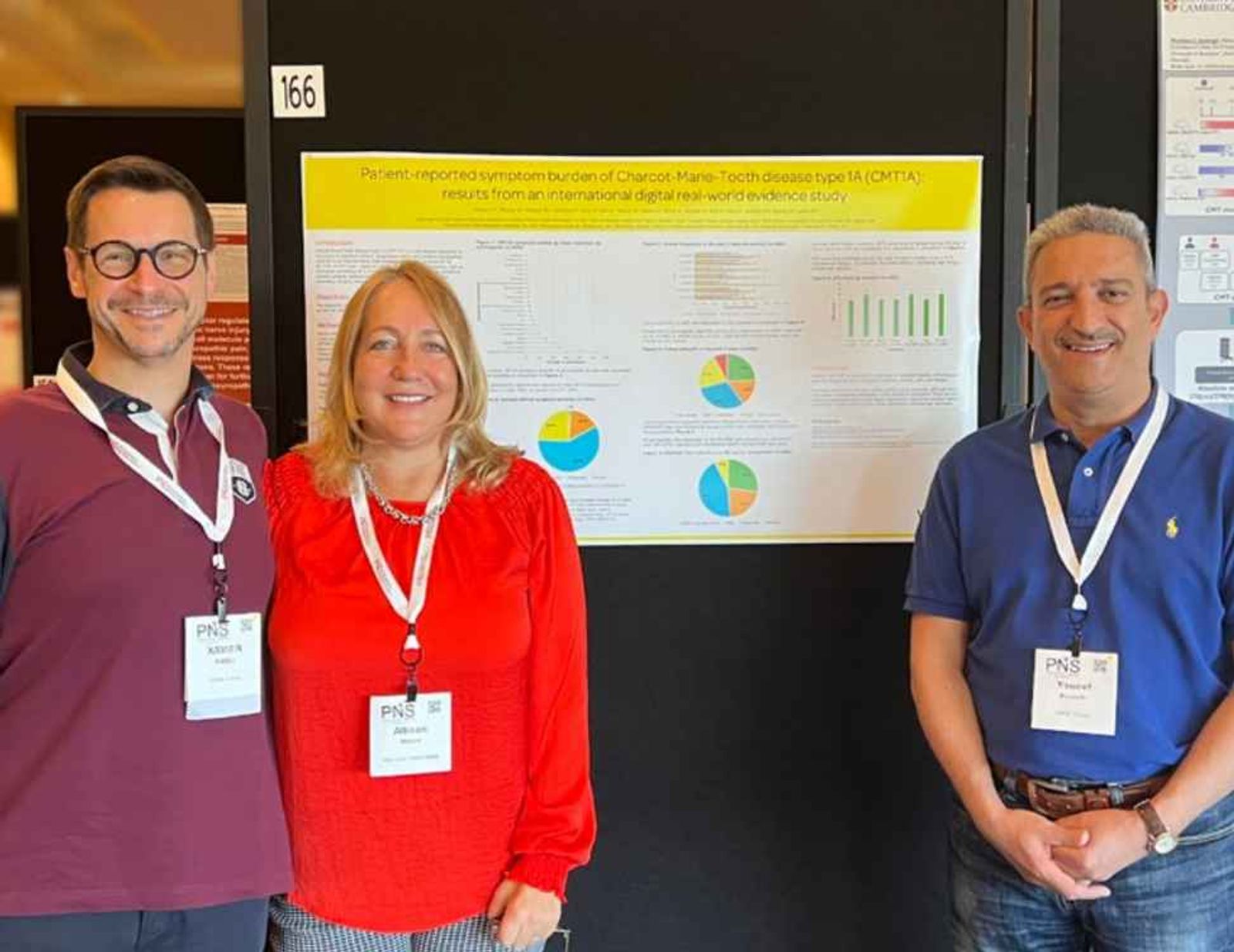 Three researchers with conference badges stand before a scientific poster presentation with charts and graphs.