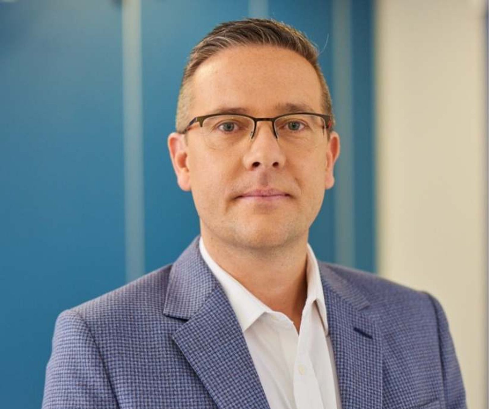 Retrato profesional de un hombre con gafas y un blazer azul, sobre un fondo de rayas azules y blancas.