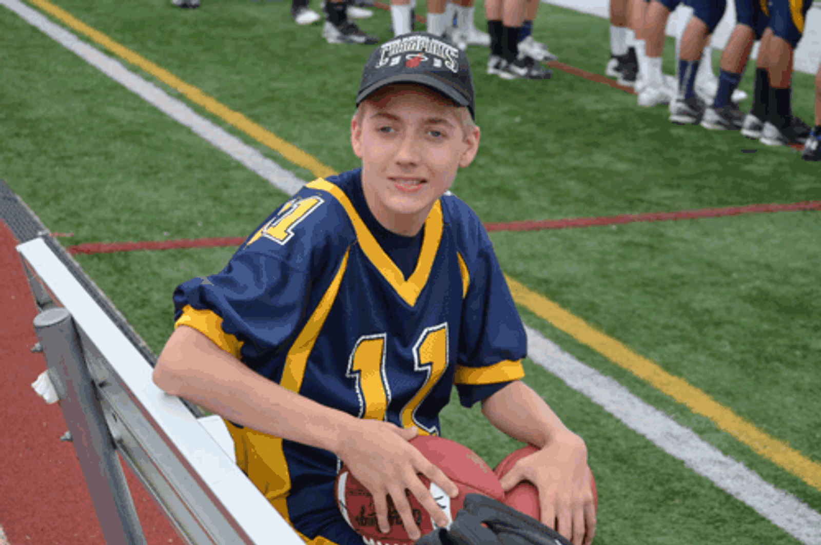 Young athlete wearing navy and gold sports uniform number 12 sitting on bleachers at field.
