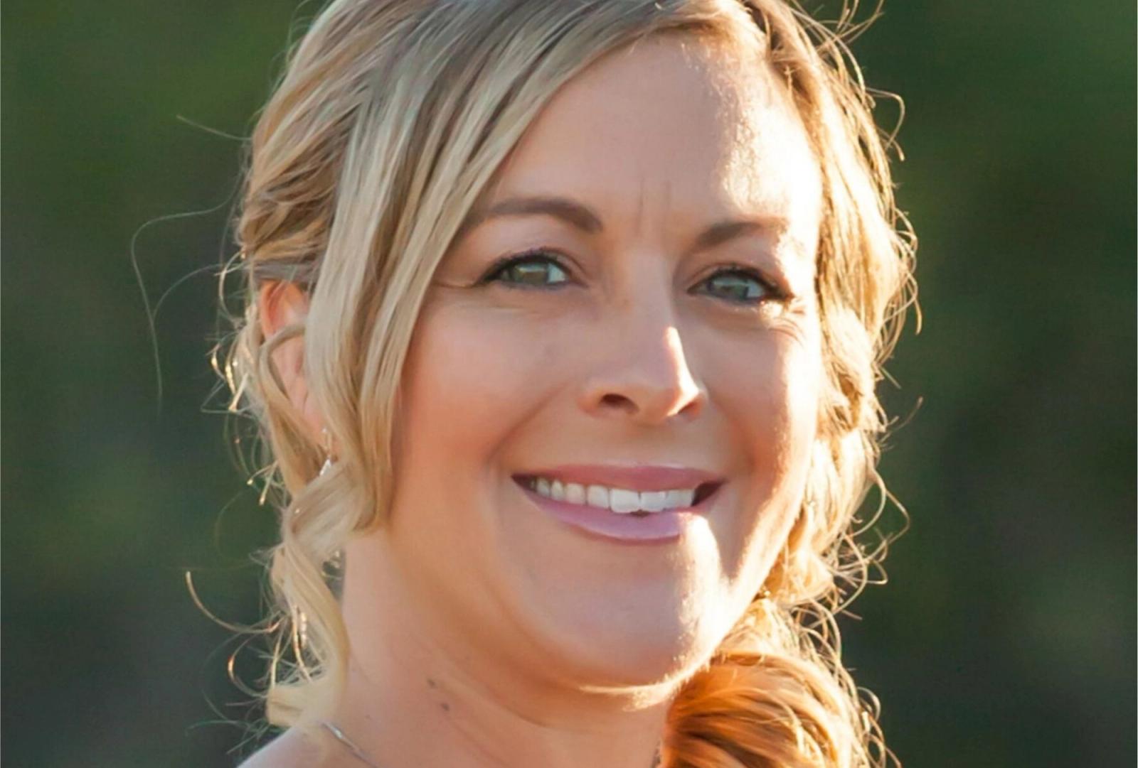 Woman with blonde hair smiling at camera against green background.