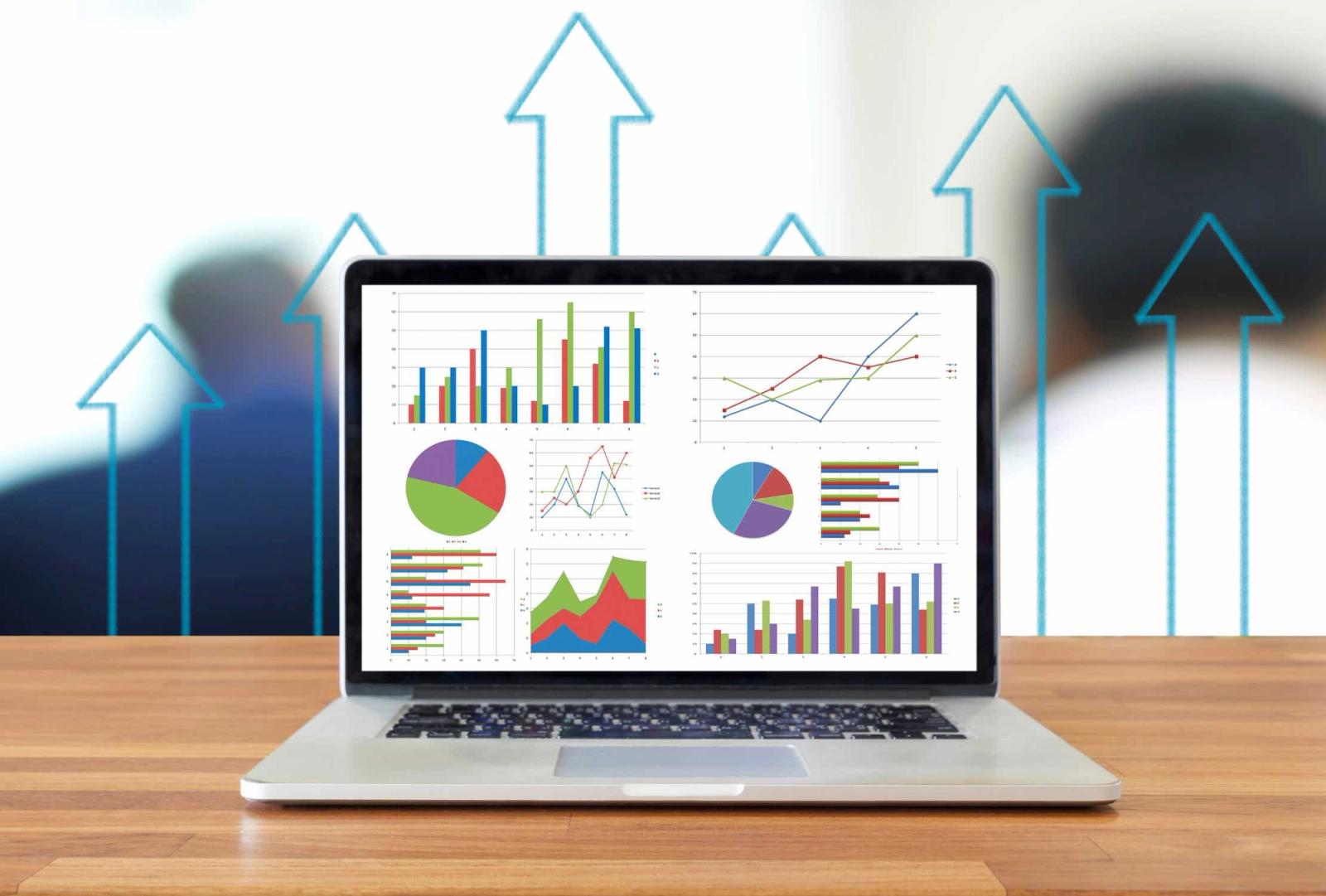 Laptop displaying various business analytics charts and graphs with upward arrow graphics in background.