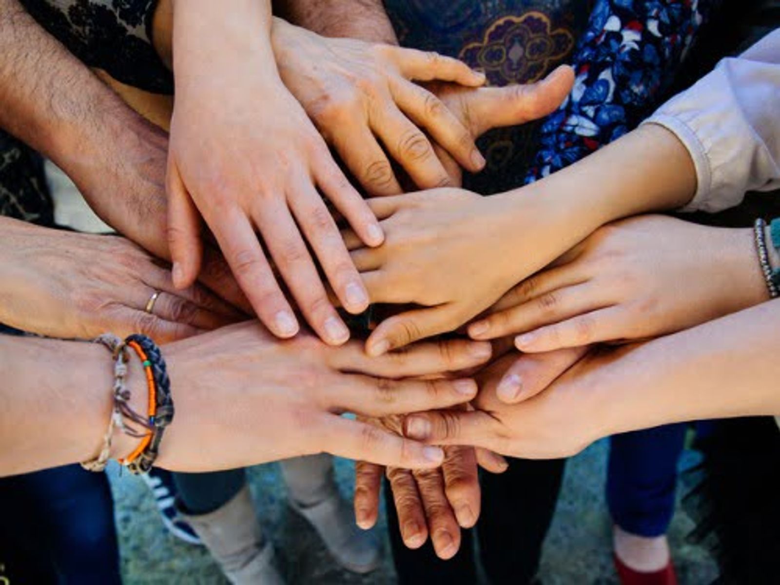 Multiple hands stacked together in a circle, showing unity and teamwork among diverse group members.
