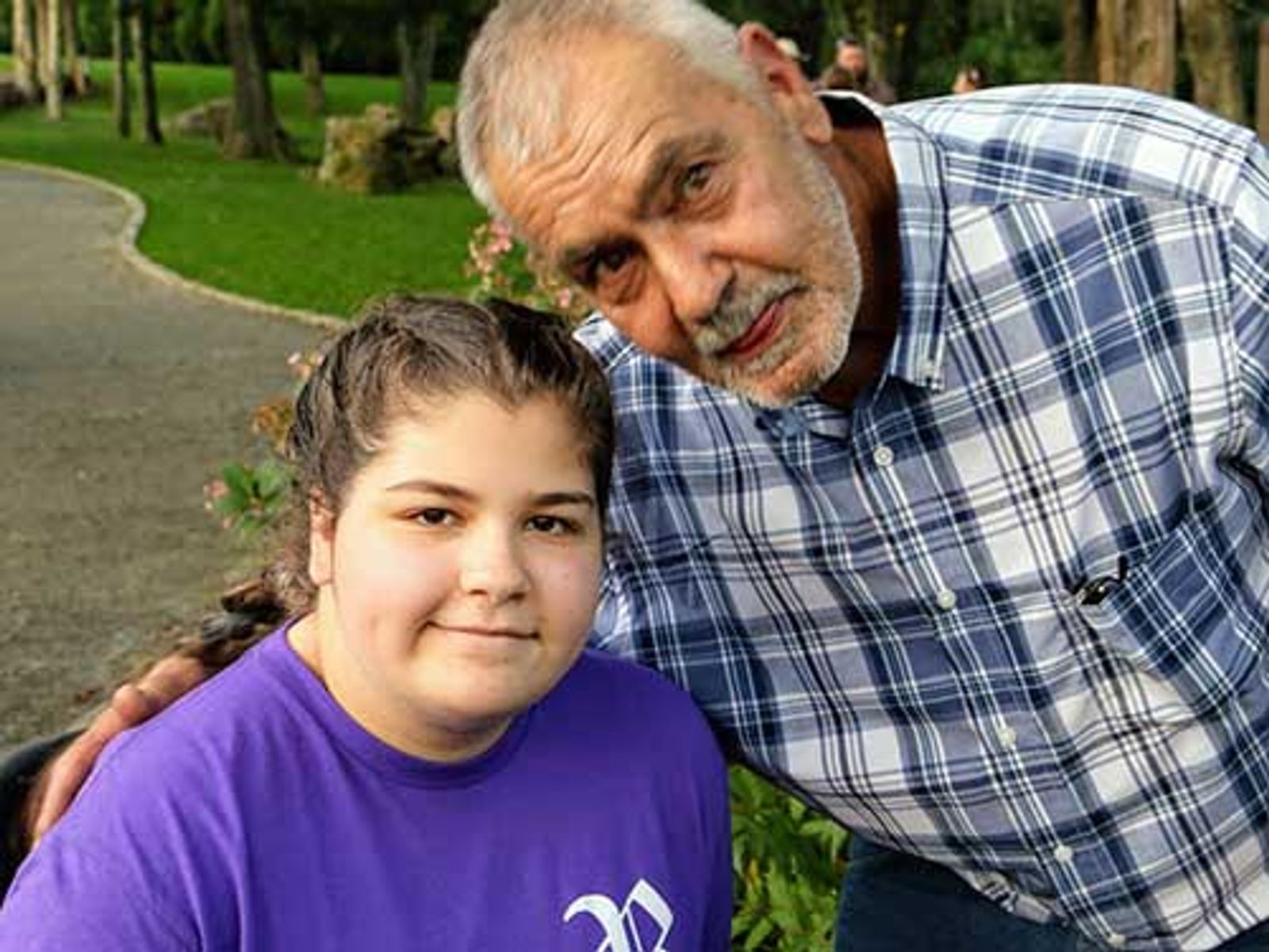 Older man and young girl smiling together outdoors in park setting.