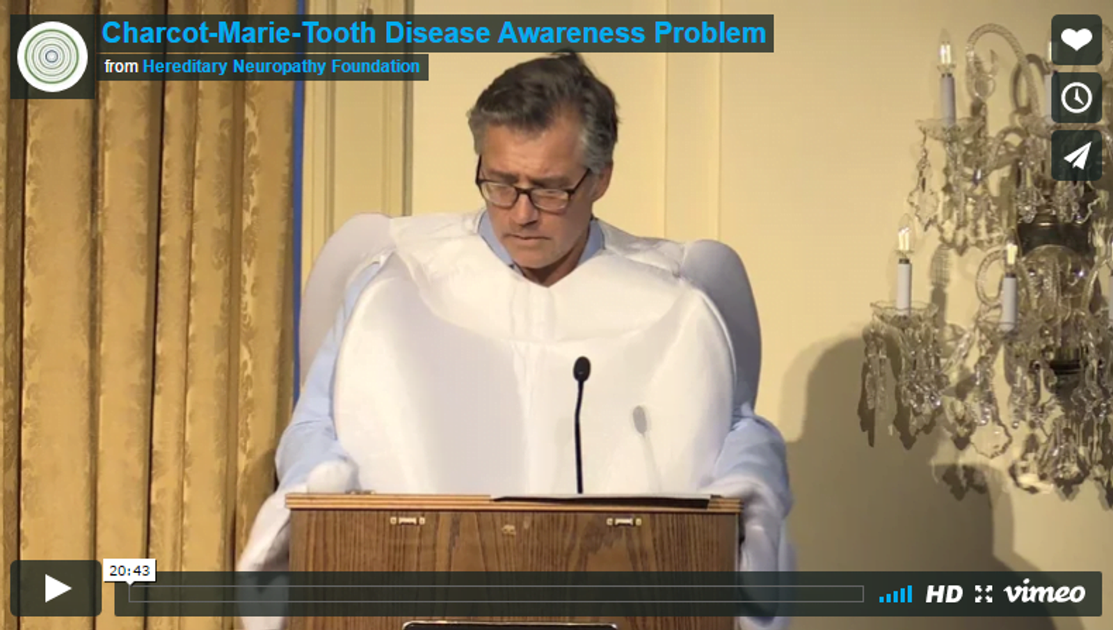 Man in white shirt speaking at podium about Charcot-Marie-Tooth Disease Awareness from Hereditary Neuropathy Foundation.