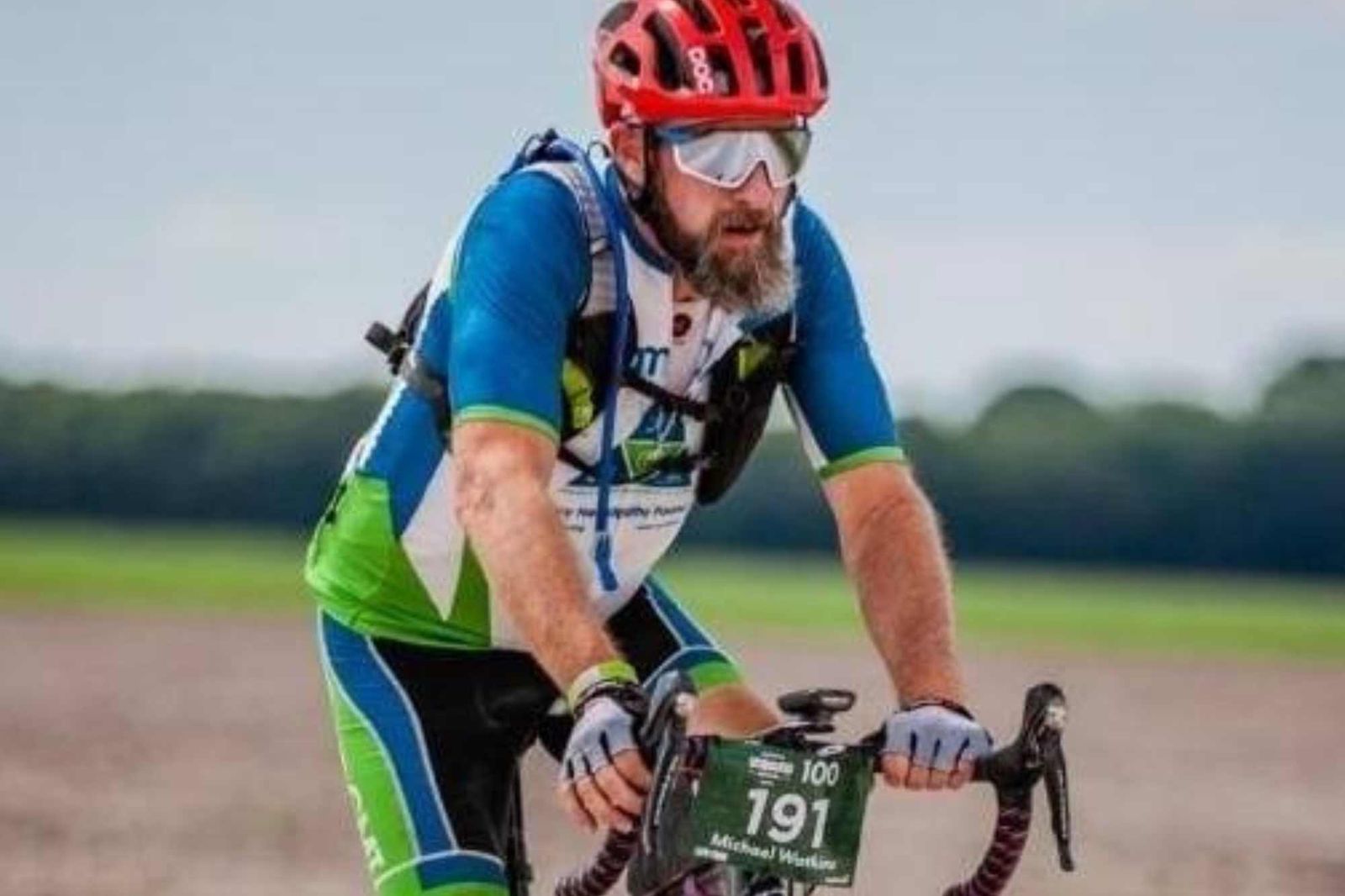 Cyclist wearing red helmet and blue jersey riding bike with race bib number 191 in open field.