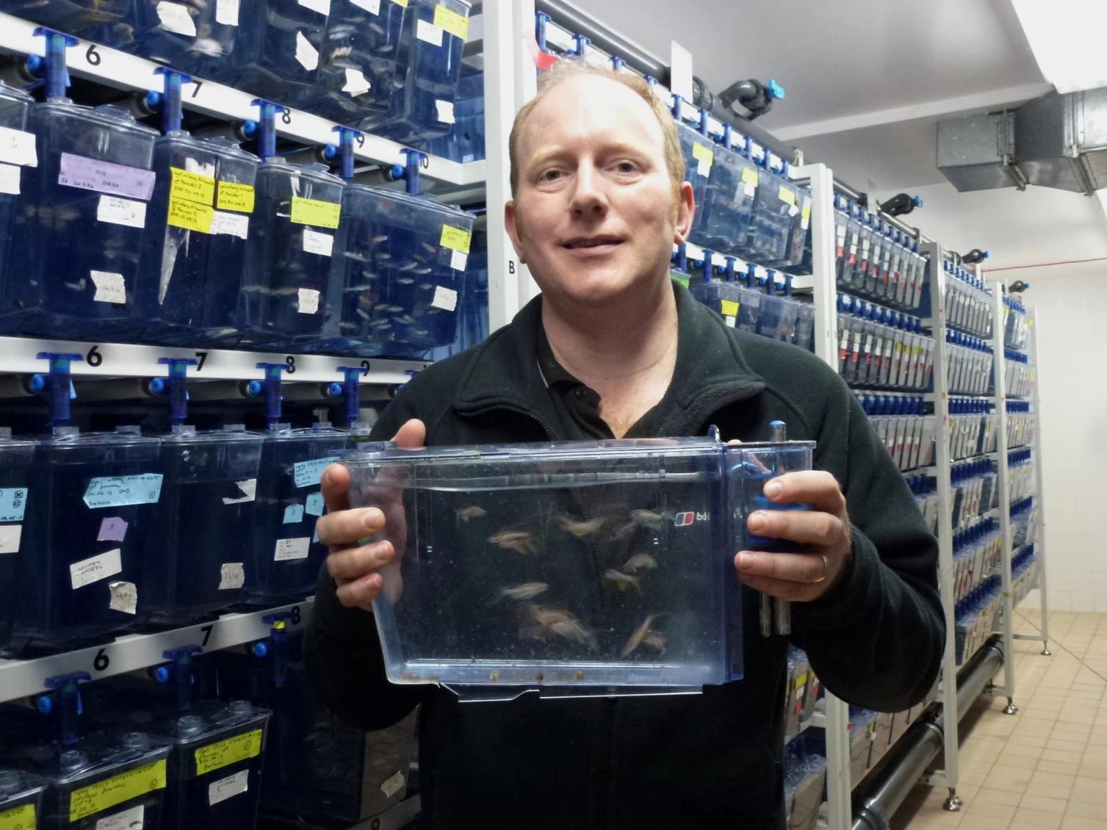 Man holding aquarium tank in front of shelving units filled with labeled storage containers.