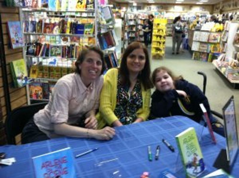 Three people at book signing table in comic book store.