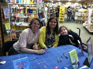 Tres personas en una mesa de firma de libros en una tienda de cómics.