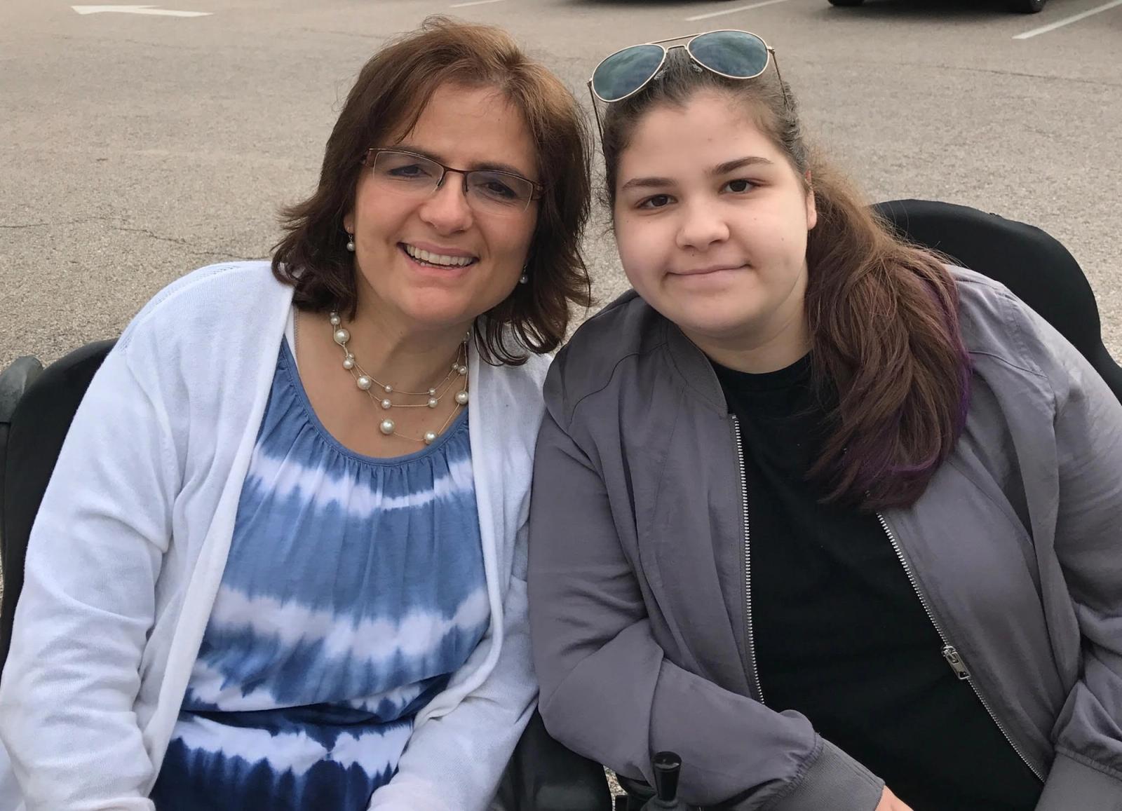 Two young women smiling at camera, seated outdoors near parked cars.