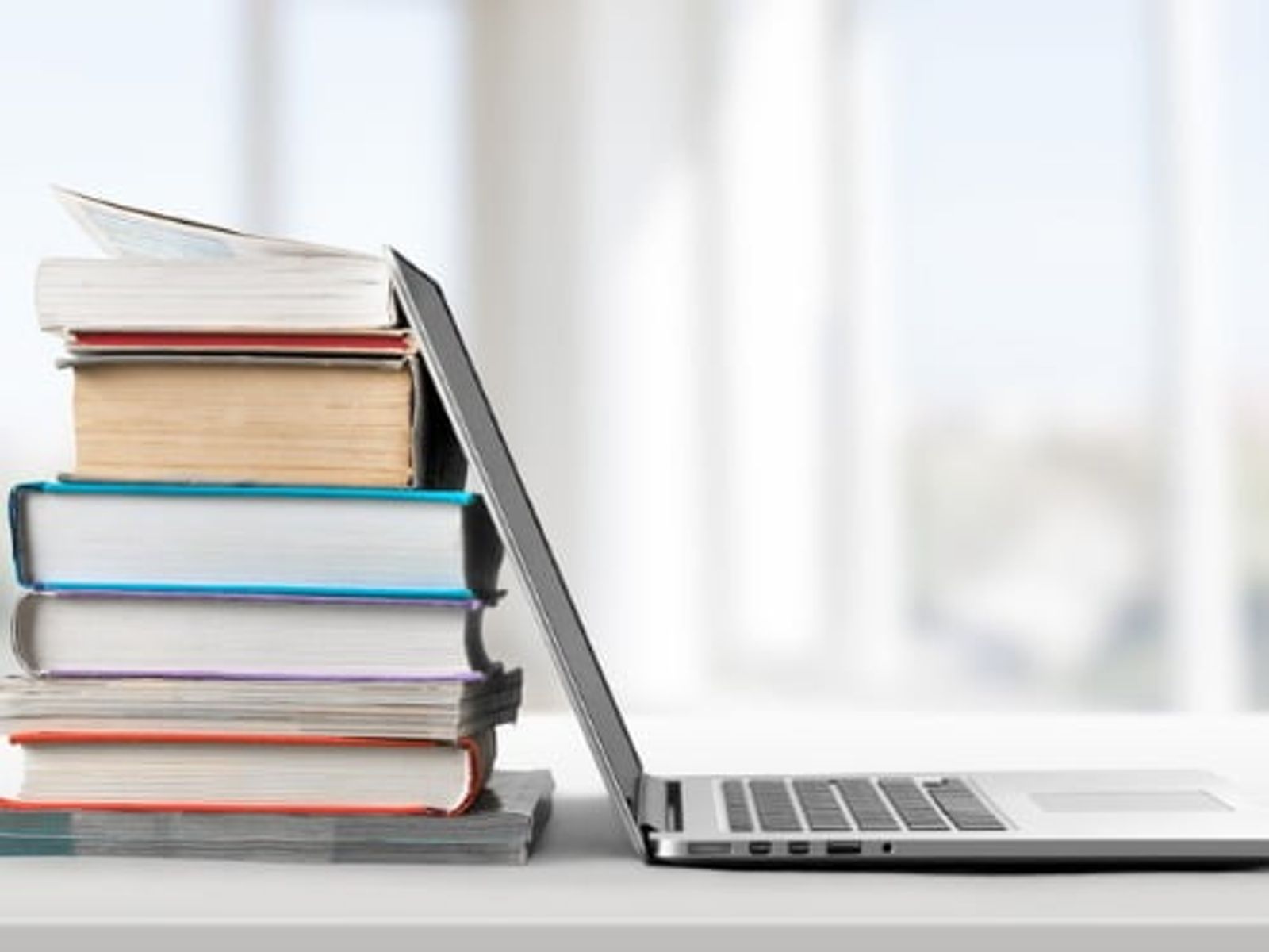 Stack of colorful books leaning against an open laptop on white desk