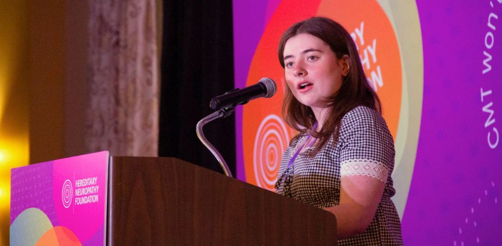 Woman speaking at podium with microphone in front of colorful backdrop displaying "CNT WOMEN"